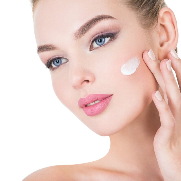 Mujer joven aplica crema cosmética en la cara.