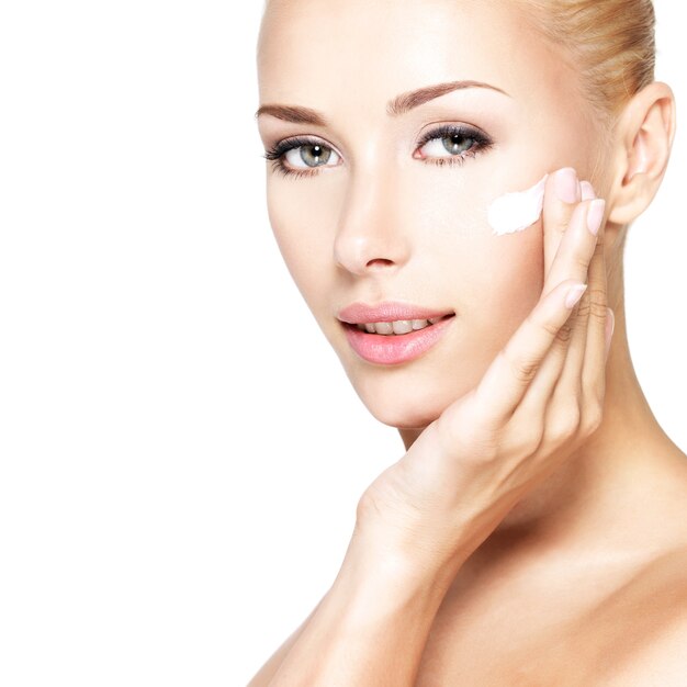 Mujer joven aplicando crema cosmética en un rostro limpio y fresco