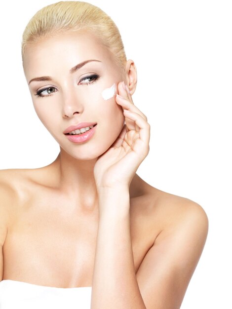 Mujer joven aplicando crema cosmética en un rostro limpio y fresco