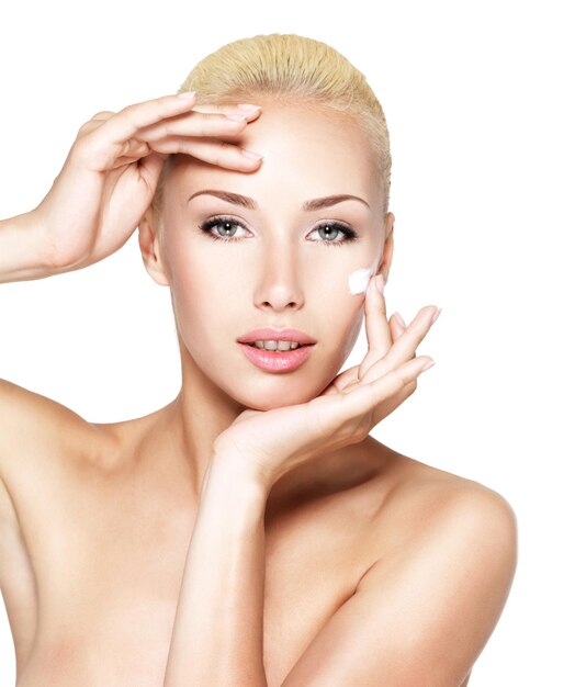 Mujer joven aplicando crema cosmética en un rostro limpio y fresco