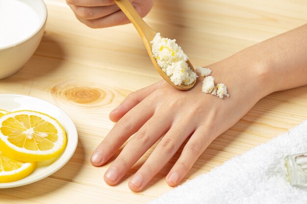 Mujer joven aplicando exfoliante de limón natural en las manos contra la mesa de madera