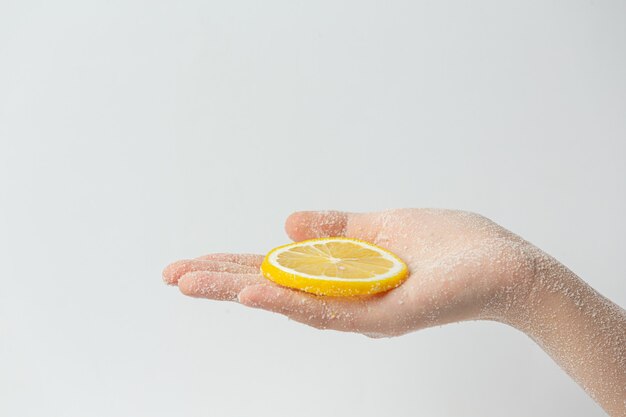 Mujer joven aplicando exfoliante de limón natural en las manos contra la superficie blanca