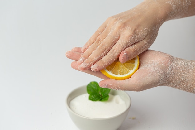 Mujer joven aplicando exfoliante de limón natural en las manos contra la superficie blanca