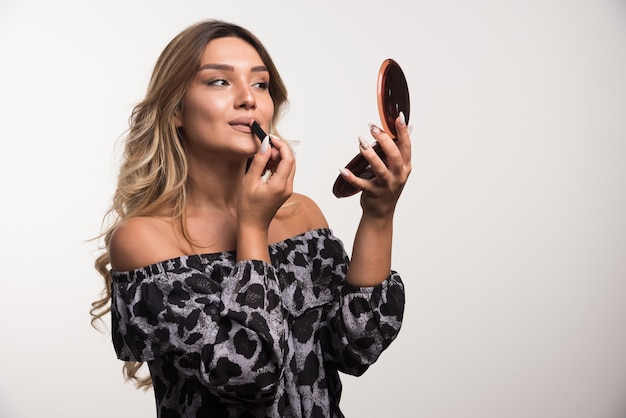 Foto gratuita mujer joven aplicando lápiz labial en la pared blanca.