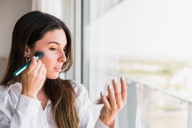 Mujer joven aplicando el polvo compacto con pincel de maquillaje