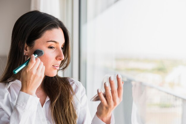 Mujer joven aplicando el polvo compacto con pincel de maquillaje