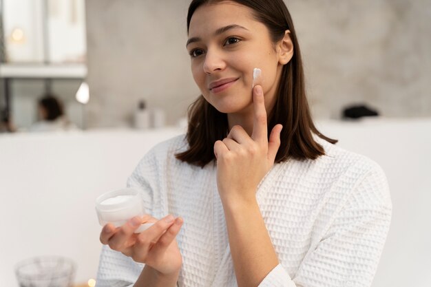 Mujer joven aplicar crema hidratante en el rostro antes de tomar un baño