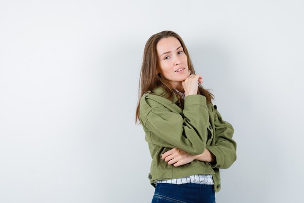 Mujer joven apoyando la barbilla en la mano en camisa, chaqueta y mirando sensible, vista frontal.