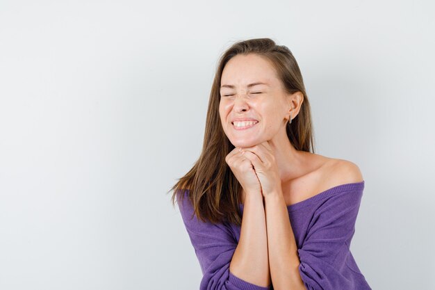 Mujer joven apoyando la barbilla en las manos entrelazadas en camisa violeta y mirando feliz. vista frontal.