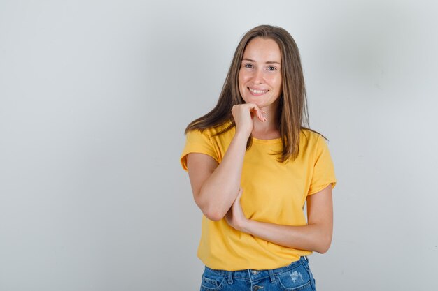 Mujer joven apoyando la barbilla en el puño en camiseta, pantalones cortos y mirando enfocado