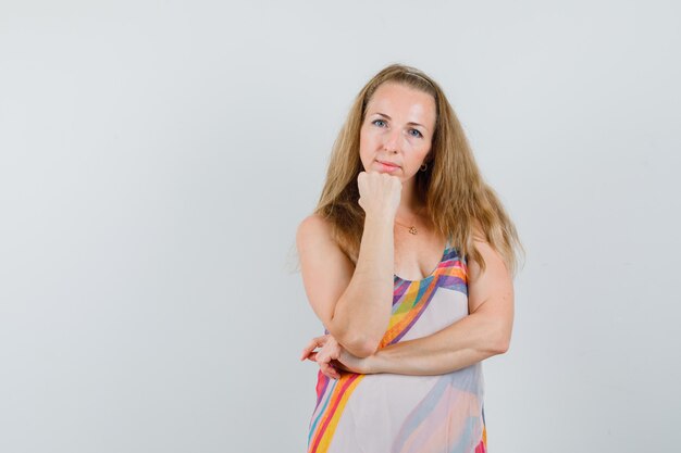 Mujer joven apoyando la barbilla en el puño en vestido de verano y luciendo sensata.