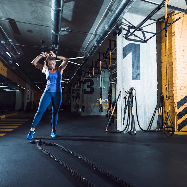 Mujer joven apta que ata su pelo en gimnasio