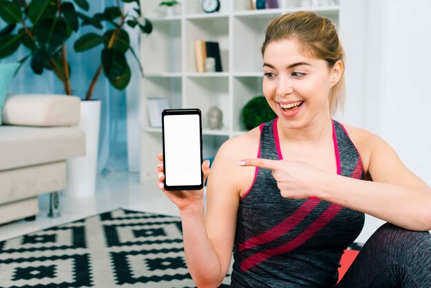 Mujer joven apta que muestra su teléfono inteligente con pantalla de visualización en blanco