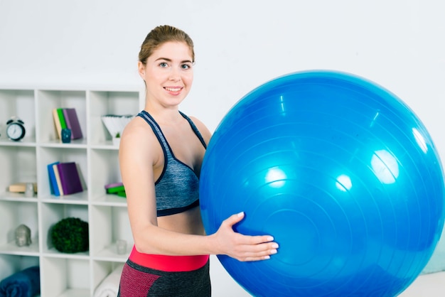 Mujer joven de la aptitud en la ropa de deportes que sostiene la bola azul grande de los pilates