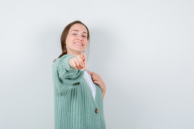 Foto gratuita mujer joven apuntando hacia adelante, manteniendo la mano en el pecho en blusa, rebeca y mirando confiado, vista frontal.