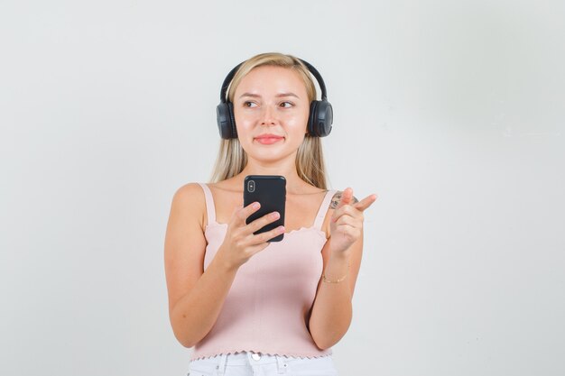 Mujer joven apuntando hacia afuera y sosteniendo el teléfono inteligente en camiseta