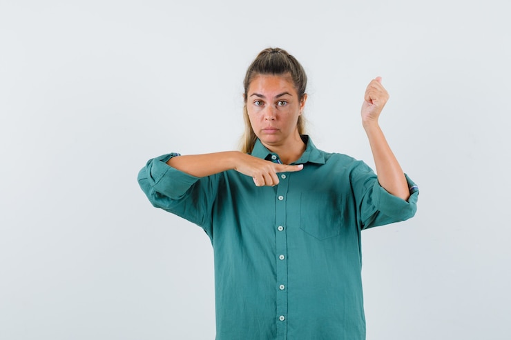 Foto gratuito mujer joven apuntando al brazo en blusa verde y mirando serio