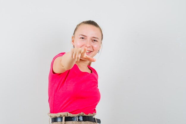 Foto gratuita mujer joven apuntando al frente en camiseta rosa y mirando feliz