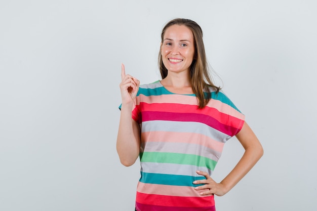 Mujer joven apuntando hacia arriba en camiseta y mirando feliz. vista frontal.