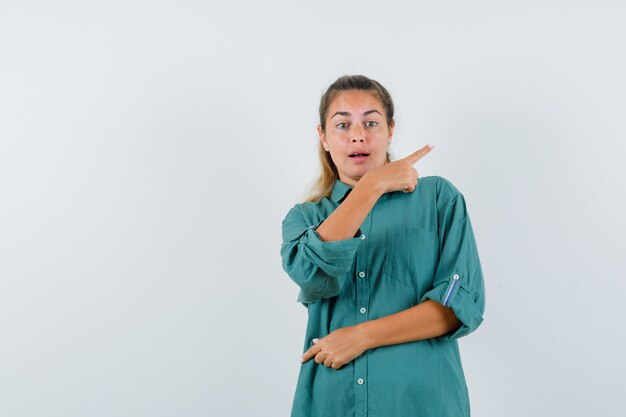 Mujer joven apuntando hacia atrás en camisa azul