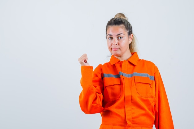 Mujer joven apuntando hacia atrás en uniforme de trabajador y mirando confiado. vista frontal.