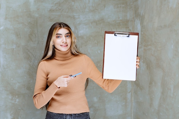 Mujer joven apuntando a un bloc de notas vacío con lápiz sobre una piedra