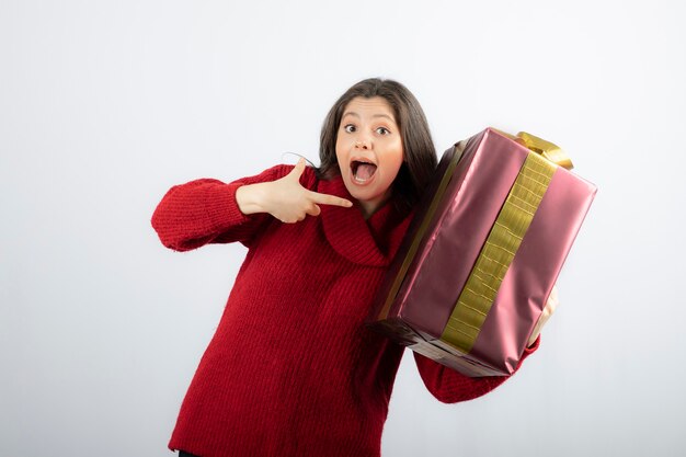 Una mujer joven apuntando a una caja de regalo de Navidad.