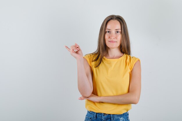 Mujer joven apuntando con el dedo en camiseta, pantalones cortos y mirando contento