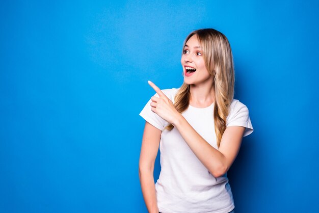 Mujer joven apuntando con el dedo hacia el lado sobre la pared azul aislada