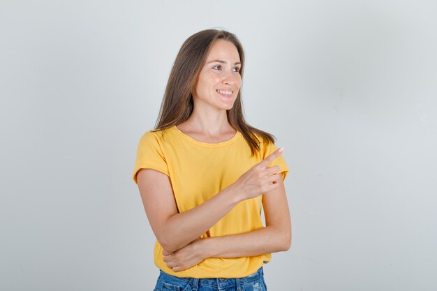 Mujer joven apuntando con el dedo a un lado y sonriendo en camiseta