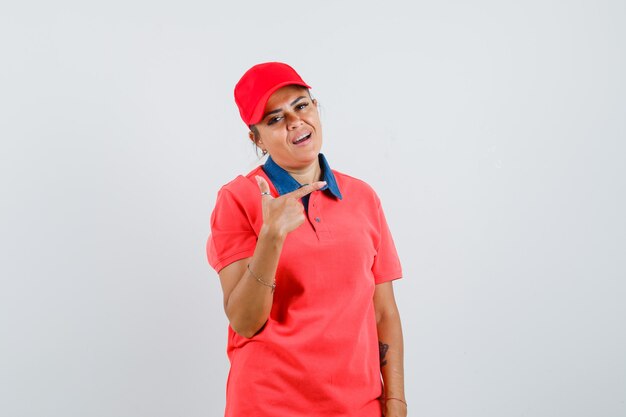 Mujer joven apuntando a la derecha con el dedo índice en camisa roja y gorra y bonita. vista frontal.