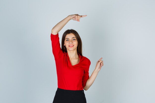 Mujer joven apuntando a la derecha con los dedos índices en blusa roja