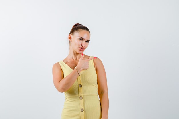 Mujer joven apuntando a la derecha en vestido amarillo y mirando indeciso