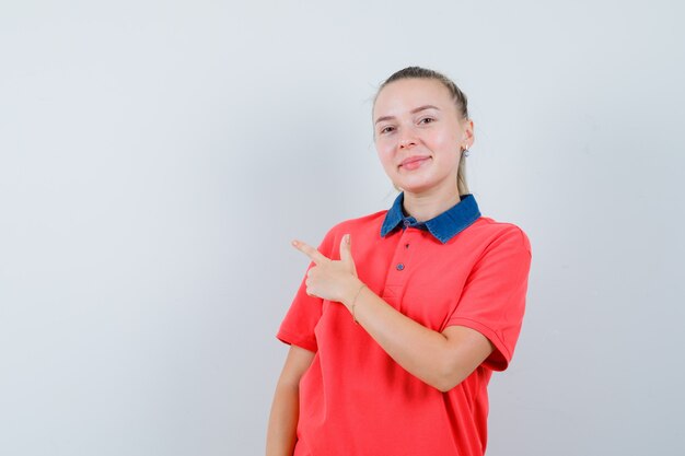 Mujer joven apuntando a la esquina superior izquierda en camiseta y mirando alegre