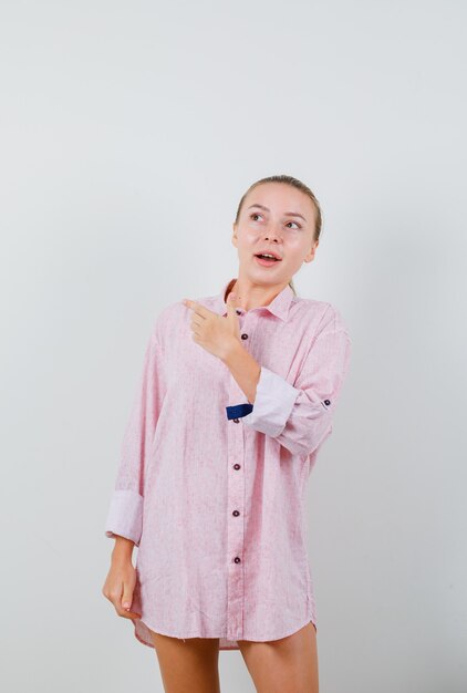 Mujer joven apuntando hacia fuera en camisa rosa y mirando curioso