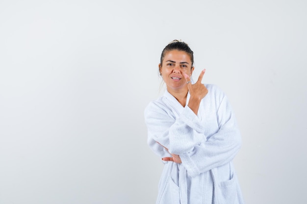 Mujer joven apuntando a un lado en bata de baño y mirando alegre