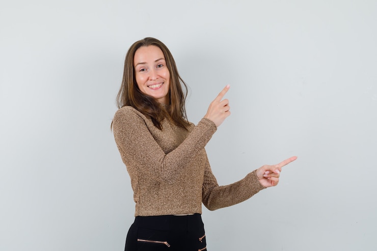 Foto gratuito mujer joven apuntando a un lado en blusa dorada y mirando positivo