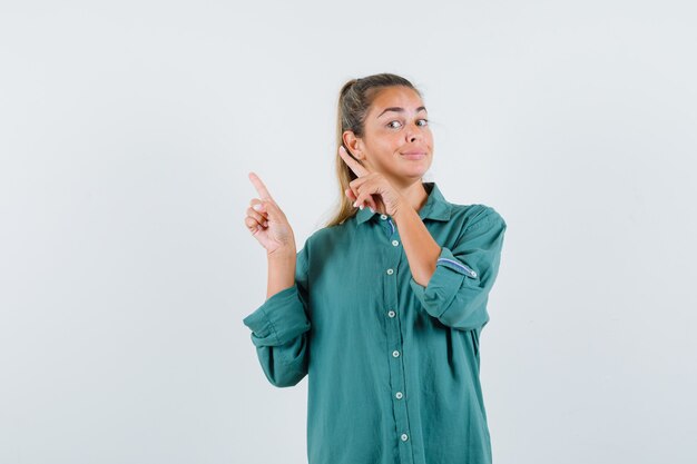 Mujer joven apuntando a un lado con camisa azul y mirando seguro