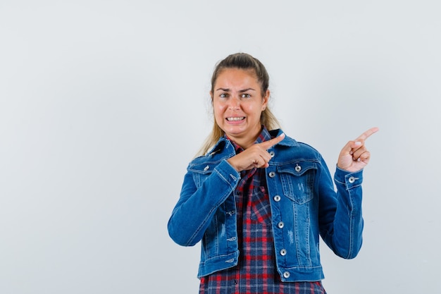 Mujer joven apuntando a un lado en camisa, chaqueta y mirando alegre. vista frontal.