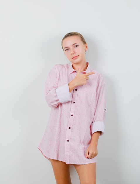 Mujer joven apuntando hacia un lado en camisa rosa y mirando disgustado