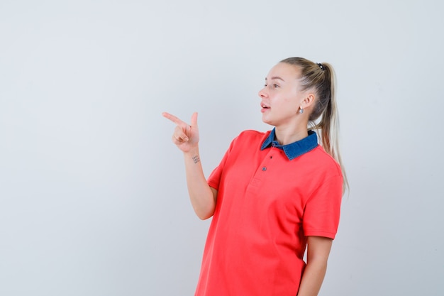 Mujer joven apuntando hacia el lado en camiseta y mirando enfocado