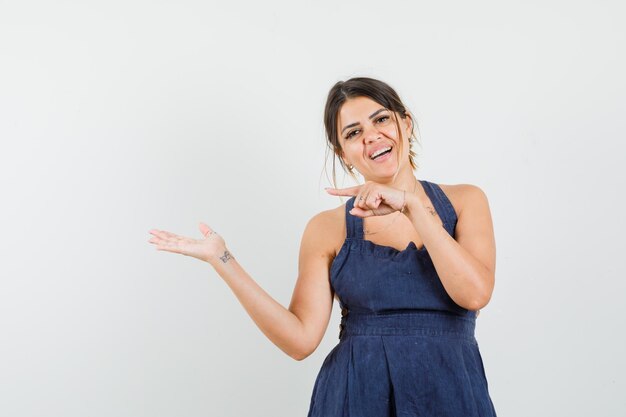 Mujer joven apuntando a un lado, extendiendo la palma en el vestido y luciendo alegre