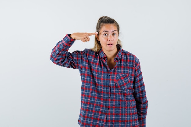 Mujer joven apuntando a sí misma con el dedo índice en camisa a cuadros y mirando seria