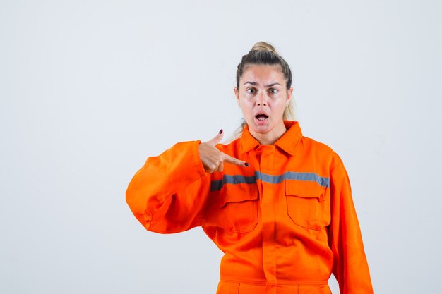 Mujer joven apuntando a sí misma en uniforme de trabajador y mirando nerviosa. vista frontal.