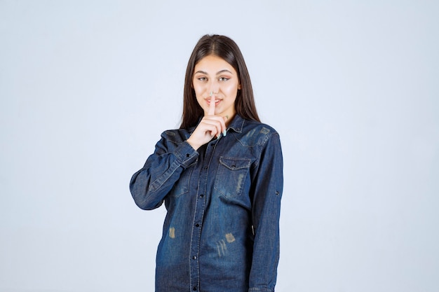 Mujer joven apuntando su boca y pidiendo silencio