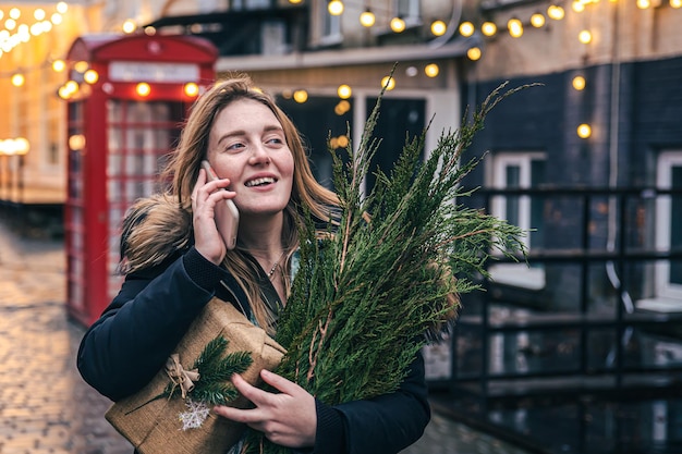 Una mujer joven con un árbol de navidad y una caja de regalo hablando por teléfono