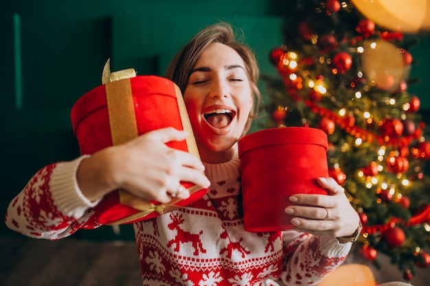 Mujer joven con árbol de Navidad con cajas rojas