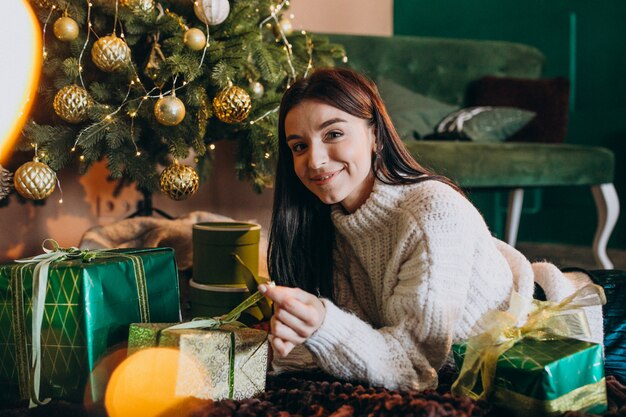 Mujer joven por árbol de navidad desempacando regalos