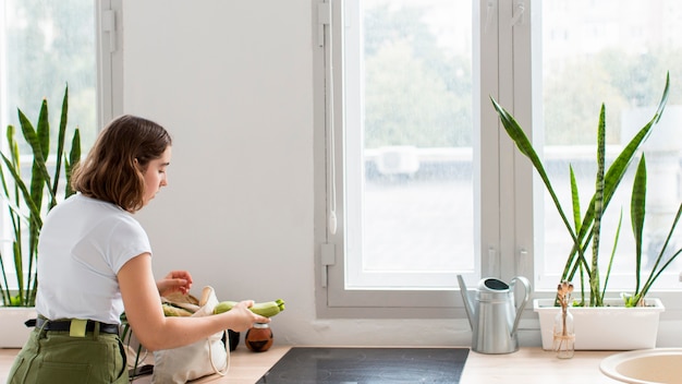 Foto gratuita mujer joven arreglando verduras orgánicas en la cocina