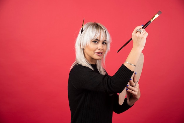 Mujer joven artista sosteniendo material de arte en una pared roja.